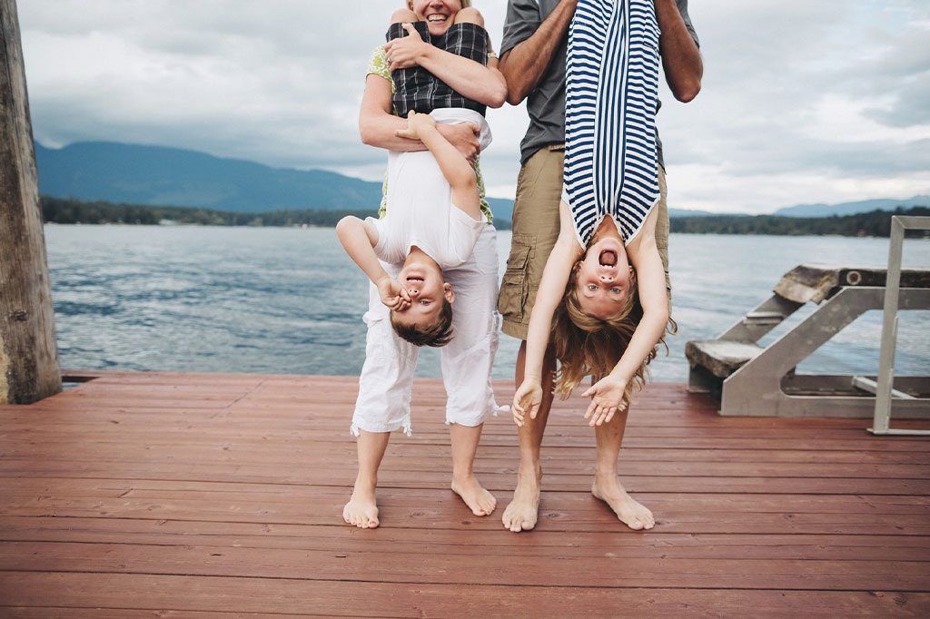 Mum and dad holding smiling daughter and son upside down on a wooden jetty